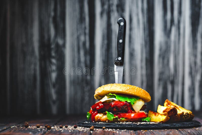Крупный план рт-мочить, очень вкусные домодельные бургеры с ножом вставил на каменной доске деревянное предпосылки темное стоковая фотография rf Крупный план рт-мочить, очень вкусные домодельные бургеры с ножом вставил на каменной доске деревянное предпосылки темное стоковая фотография rf