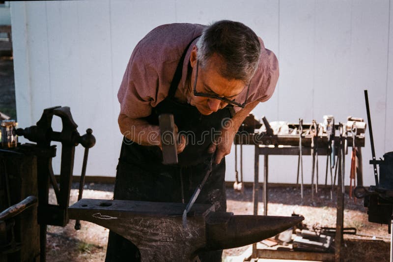 A blacksmith working on a glowing piece of metal above an anvil at the Hopkinton Fair. Hopkinton New Hampshire. The image was captured on analog color film. A blacksmith working on a glowing piece of metal above an anvil at the Hopkinton Fair. Hopkinton New Hampshire. The image was captured on analog color film