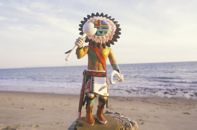 Hopi Kachina doll holding objects on beach with ocean in the background. Hopi Kachina doll holding objects on beach with ocean in the background