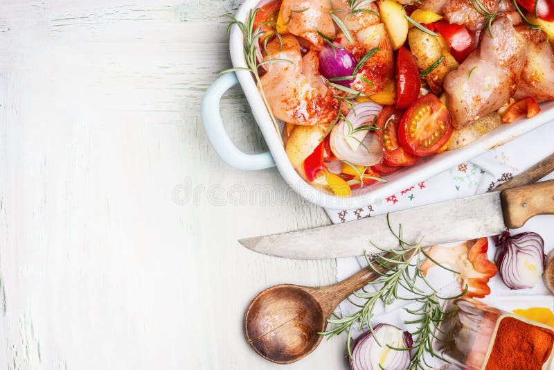 Куриная грудка с овощами отрезка красочными в покрытом эмалью сотейнике с деревянными ложкой и кухонным ножом на белой деревянной стоковое фото rf