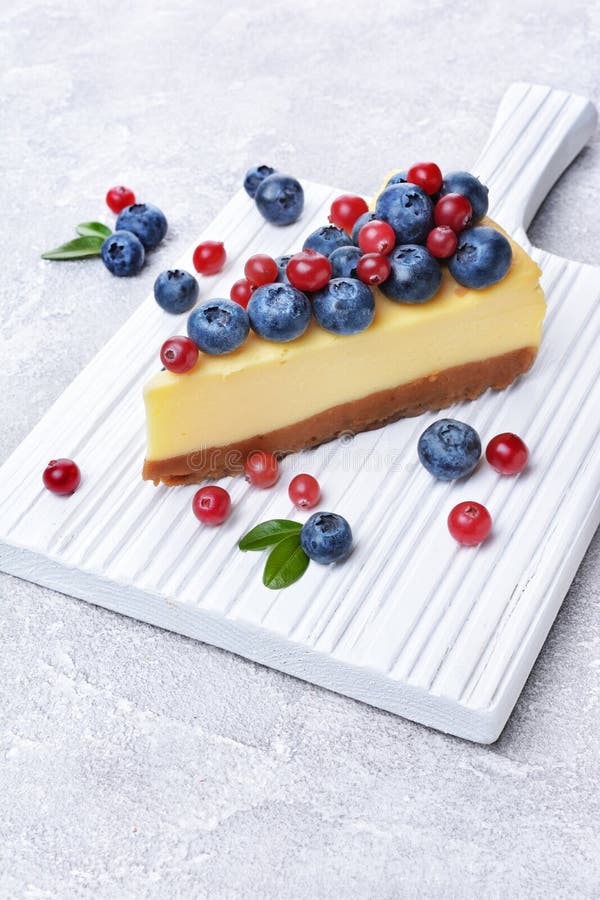 Кусок конца-вверх очень вкусного домодельного чизкейка с свежими голубиками и клюквами на белой деревянной разделочной доске стоковая фотография rf Кусок конца-вверх очень вкусного домодельного чизкейка с свежими голубиками и клюквами на белой деревянной разделочной доске стоковая фотография rf
