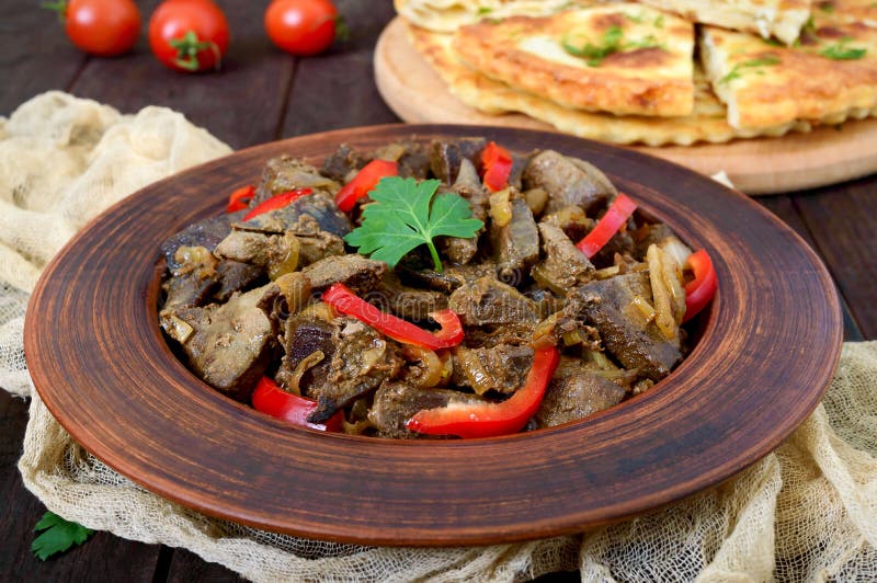 кусочки жареной печени с луком и свежими колокольчиками на тарелке. стоковое изображение