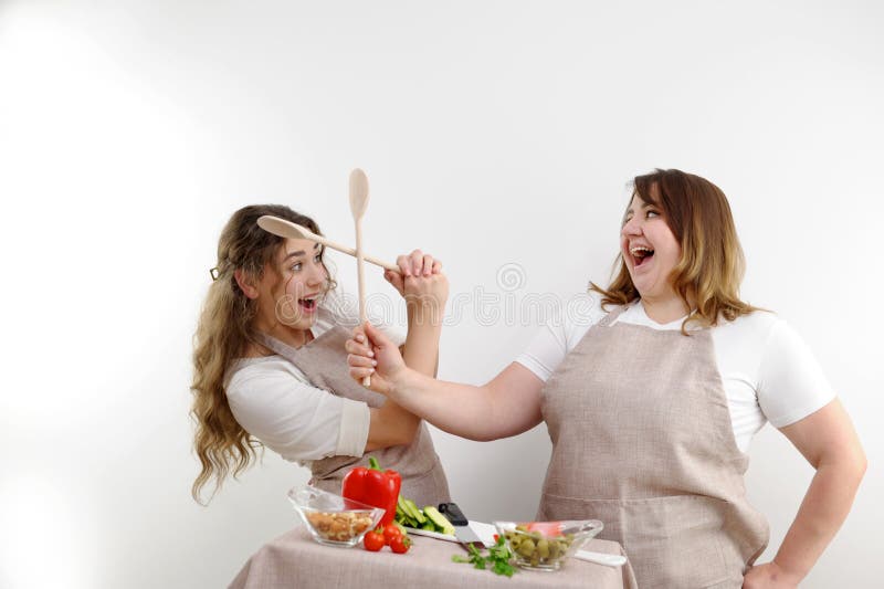 kitchen people fight 2 cheerful women fighting with wooden spoons on white background fun concept of cooking healthy food. kitchen people fight 2 cheerful women fighting with wooden spoons on white background fun concept of cooking healthy food