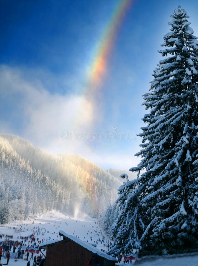 Scenic view of colorful rainbow over forested mountainside and ski slope, winter scene. Scenic view of colorful rainbow over forested mountainside and ski slope, winter scene.