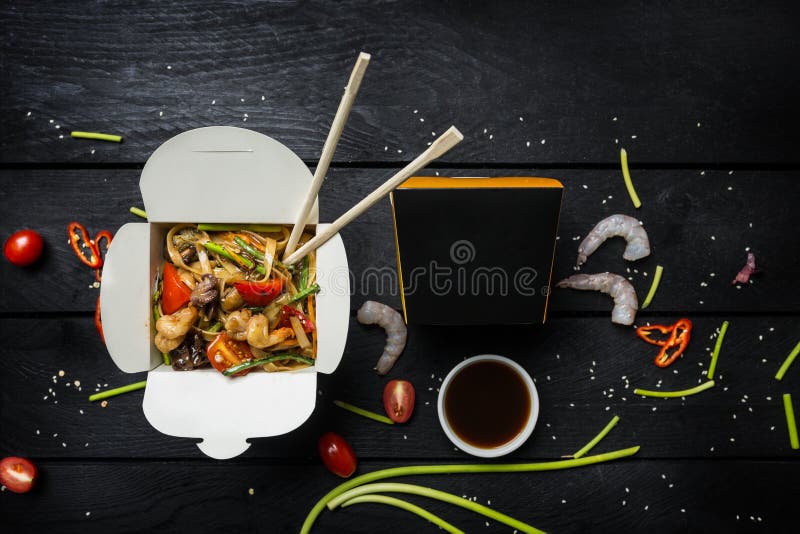 Лапши фрая stir Udon с морепродуктами в коробке на черной предпосылке С палочками и коробкой для лапшей стоковое изображение rf Лапши фрая stir Udon с морепродуктами в коробке на черной предпосылке С палочками и коробкой для лапшей стоковое изображение rf