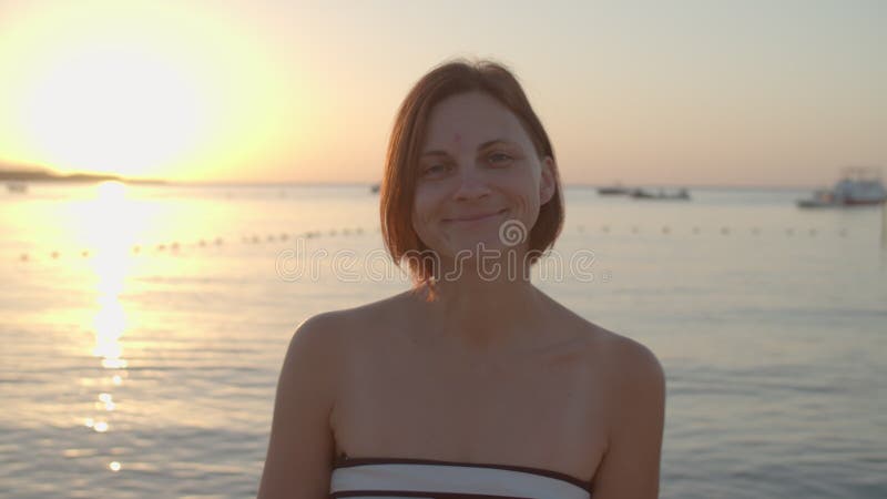 30-летняя женщина в купальнике, идущая к морю, повернулась к камере и улыбнулась. Женщина наслаждается рассветом на пляже. вид сза сток-видео