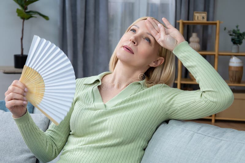 50-летняя женщина, которая сидит с вентилятором в руке и страдает от жары стоковое изображение