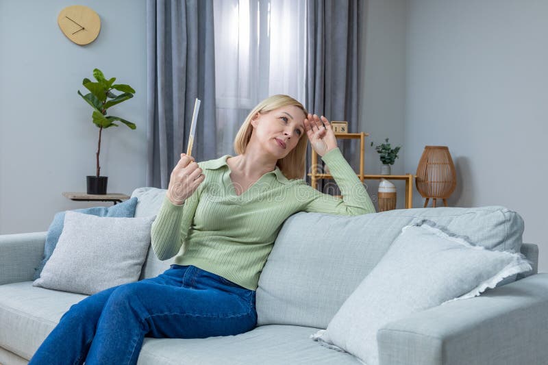 50-летняя женщина, которая сидит с вентилятором в руке и страдает от жары стоковое фото