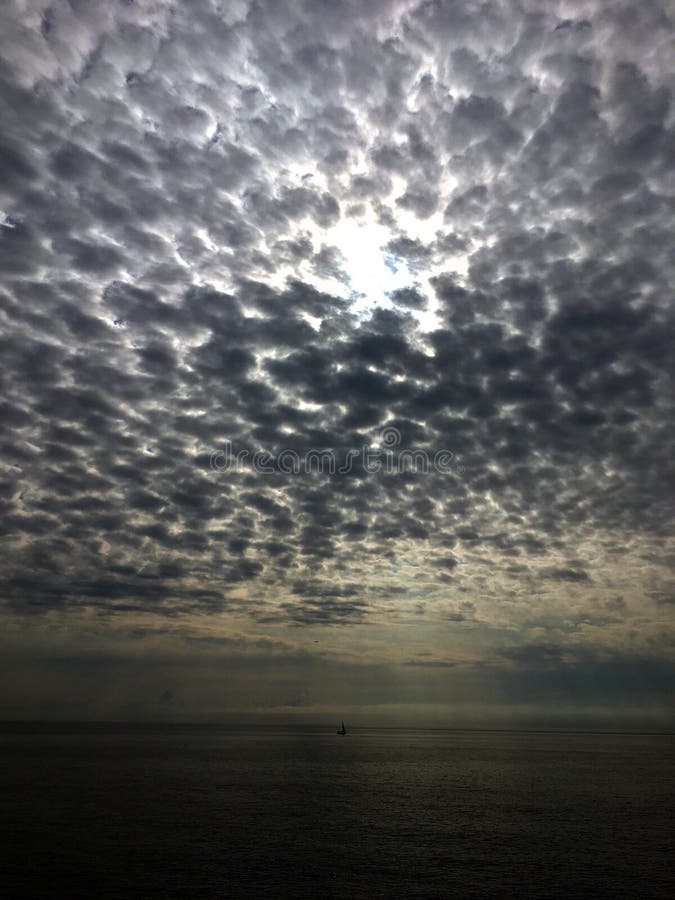 Лучи облачного неба и солнца над морем со шлюпкой стоковые фотографии rf Лучи облачного неба и солнца над морем со шлюпкой стоковые фотографии rf
