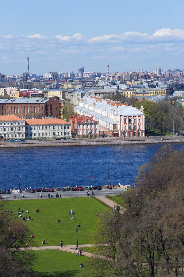 Люди имея остатки на зеленой лужайке на банке реки Neva, pe St стоковое изображение rf Люди имея остатки на зеленой лужайке на банке реки Neva, pe St стоковое изображение rf