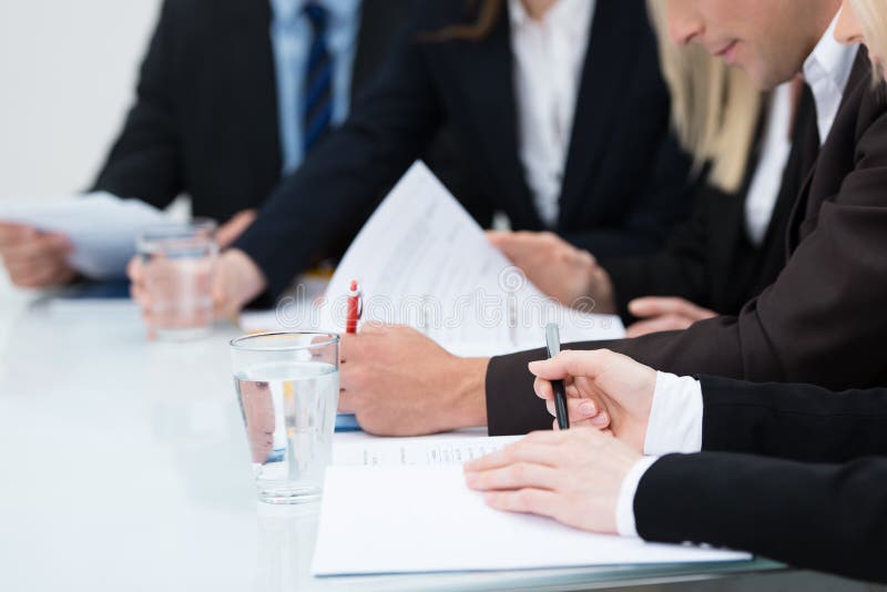 Close up view of the hands of business people taking notes in a meeting seated at a table. Close up view of the hands of business people taking notes in a meeting seated at a table