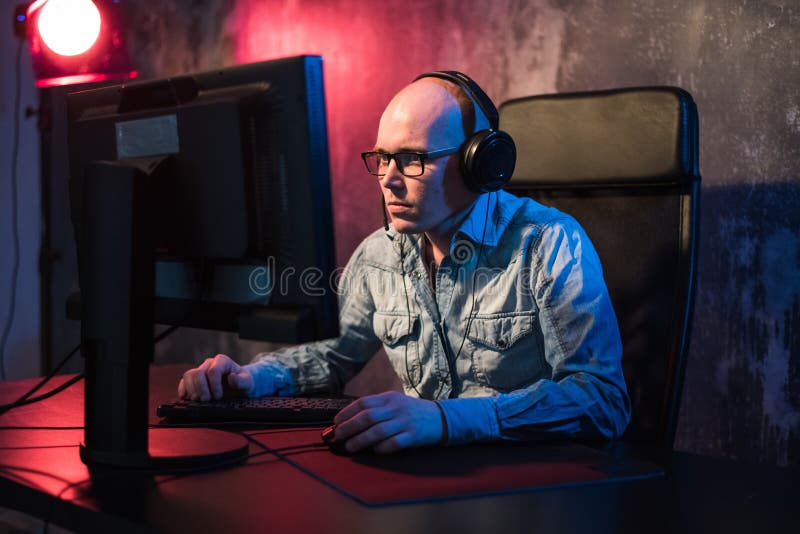 Любимое хобби Выборочный профиль сконцентрированного молодого gamer в наушниках сидит в клубе компьютера Игра виртуальная стоковое изображение Любимое хобби Выборочный профиль сконцентрированного молодого gamer в наушниках сидит в клубе компьютера Игра виртуальная стоковое изображение