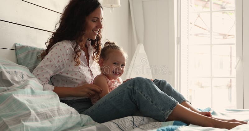 любящая латина мама щекочет обнимать маленькую девочку на кровати