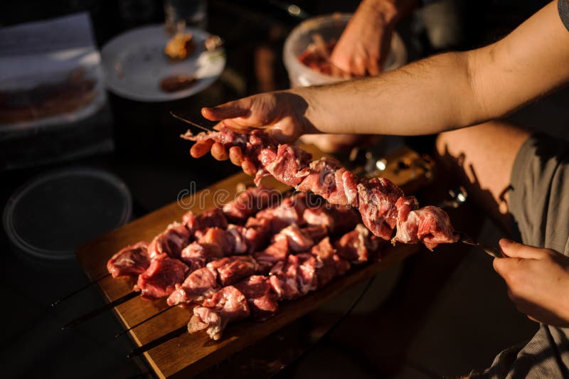 Люди шнуруя части свежего мяса на стальных протыкальниках стоковое изображение rf Люди шнуруя части свежего мяса на стальных протыкальниках стоковое изображение rf