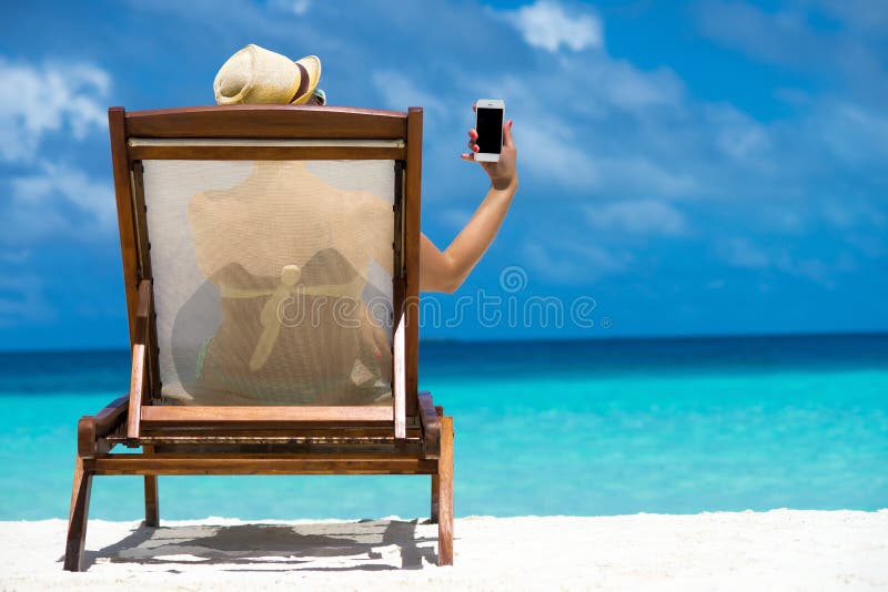Маленькая девочка лежа на lounger пляжа с мобильным телефоном в руке стоковое фото rf Маленькая девочка лежа на lounger пляжа с мобильным телефоном в руке стоковое фото rf