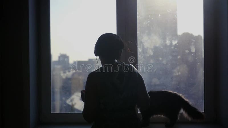 Маленькая девочка слушает к музыке на наушниках, танцам, кот сидит на windowsill и смотрит хозяйку Slowmotion