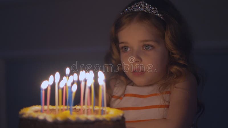 Маленькая девочка смотрит именниный пирог и делает желание перед дуть вне свечи