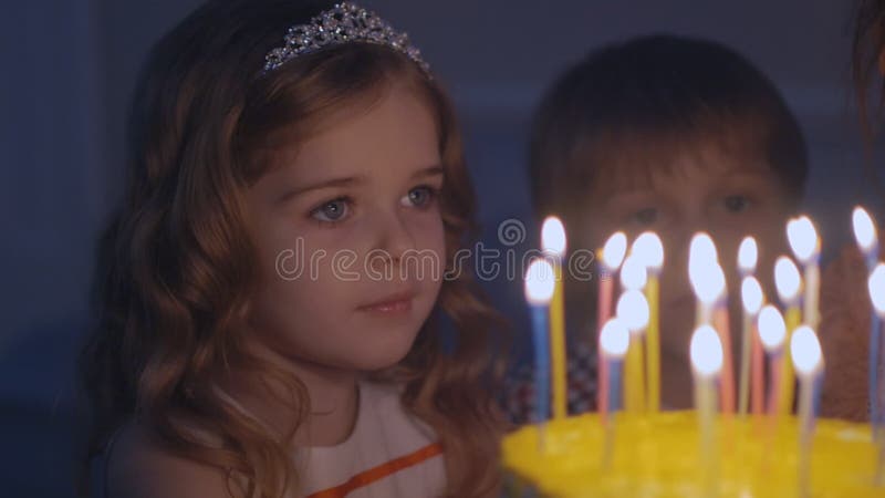 Маленькая девочка смотрит свечи на праздничном торте и делает желание в замедленном движении