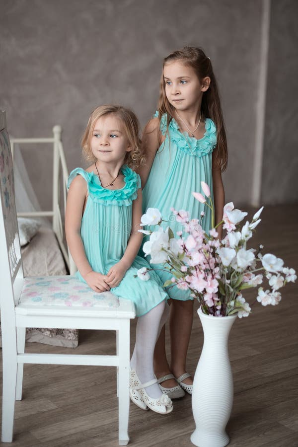 2 little girls in white dresses sitting in looking at you. 2 little girls in white dresses sitting in looking at you