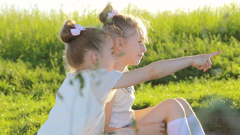 2 маленькой девочки сидя на говорить травы имеют потеху