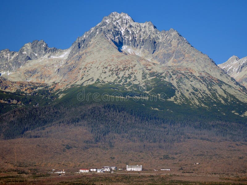 Autumn view of small buildings under huge Gerlach peak. This peak is with its altitude of 2,655 meters the highest peak of High Tatra Mountains as well as the highest peak in the whole 1,500 kilometers long Carpathian mountain chain. It belongs to High Tatras national park, TANAP. Autumn view of small buildings under huge Gerlach peak. This peak is with its altitude of 2,655 meters the highest peak of High Tatra Mountains as well as the highest peak in the whole 1,500 kilometers long Carpathian mountain chain. It belongs to High Tatras national park, TANAP.