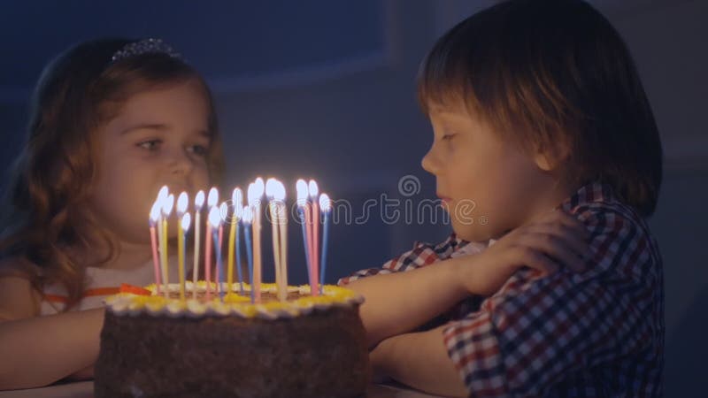Мальчик и девушка на праздничном торте смотрят свечи и делают желания