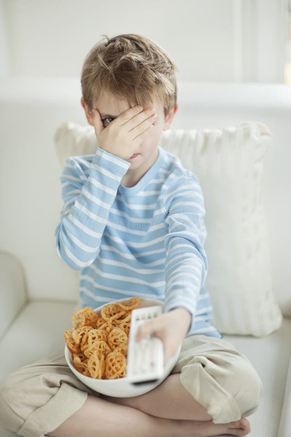 Мальчик смотря страшное кино с шаром полным лепешек закуски формы колеса