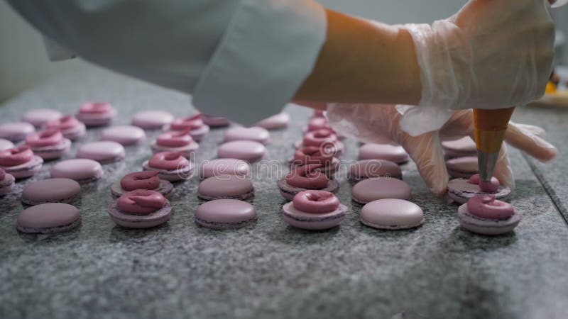 Магазин конфеты Украшение французских macaroons Работник магазина конфеты в перчатках добавляет сливк и ягоды к готовому