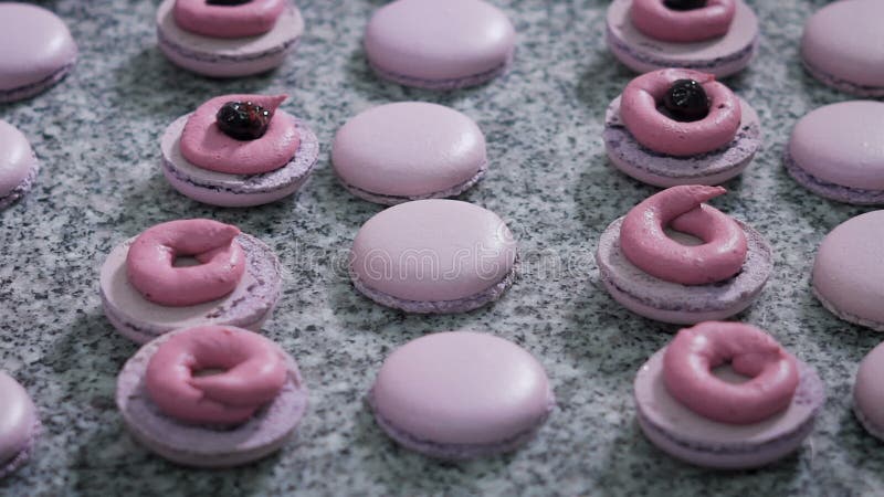 Магазин конфеты Украшение французских macaroons Работник магазина конфеты в перчатках добавляет сливк и ягоды к готовому