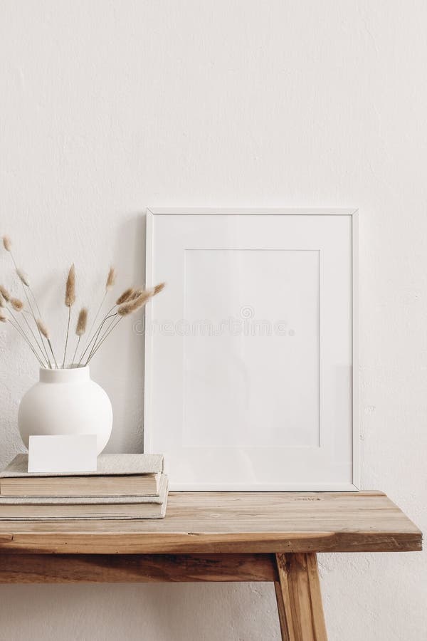 Portrait white picture frame mockup on vintage bench, table. Modern ceramic vase with dry Lagurus ovatus grass, books and busines card. White wall background. Scandinavian interior, vertical. Portrait white picture frame mockup on vintage bench, table. Modern ceramic vase with dry Lagurus ovatus grass, books and busines card. White wall background. Scandinavian interior, vertical.