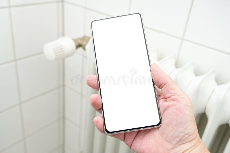 макет руки, держащий смартфон с пустым белым дисплеем перед концепцией радиатора нагревателя для повышения стоимости энергии стоковое изображение rf