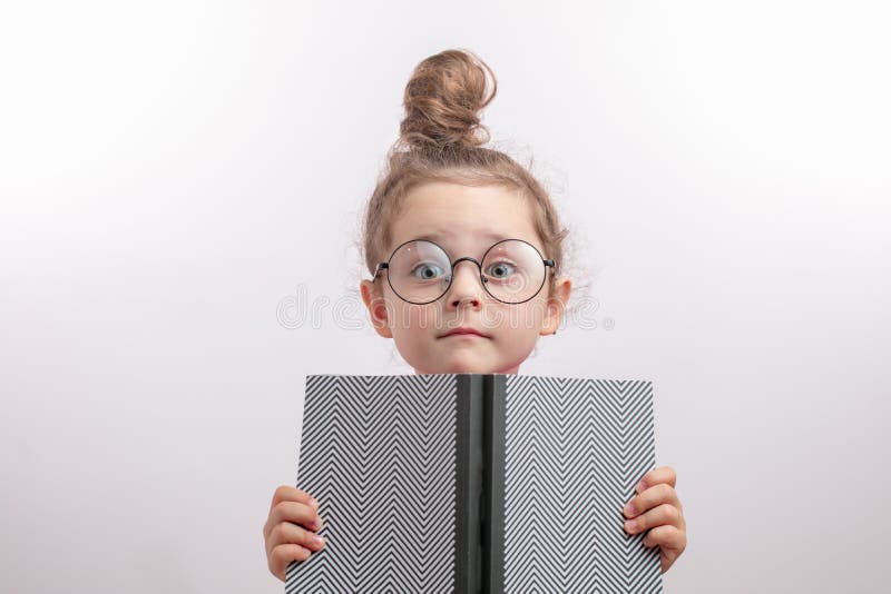 Маленькая девочка с hairbun доверяя вне ее голове от раскрытой книги стоковые изображения rf Маленькая девочка с hairbun доверяя вне ее голове от раскрытой книги стоковые изображения rf