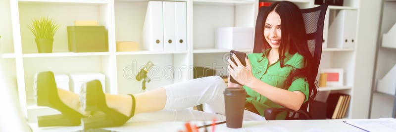 Маленькая девочка сидит в офисе, бросила ее ноги на таблице и держит телефон в ее руках стоковые фото