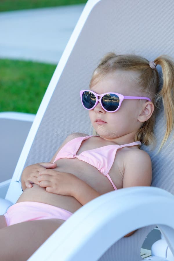 Маленькая девочка со светлыми волосами отдыхает на lounger Ребенок положил дальше его солнечные очки Фотография лета стоковое фото