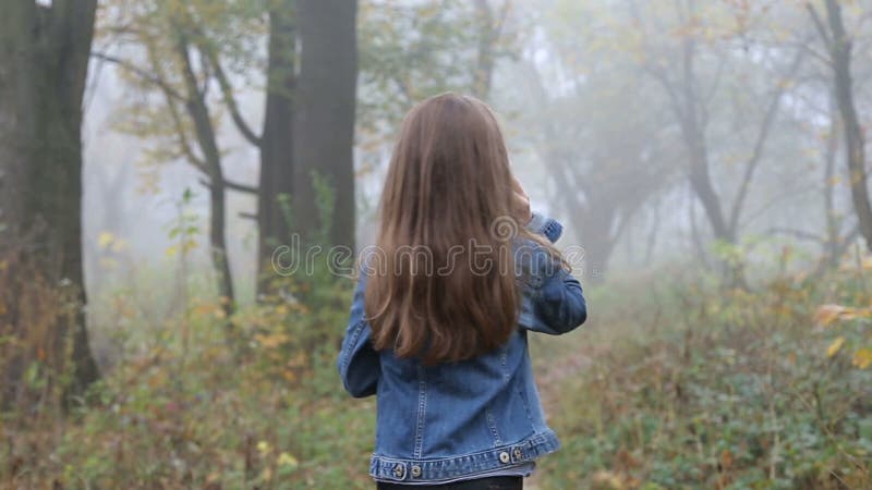 Маленькая европейская девушка с длинными волосами, синим пиджаком, черными брюками, тапками и голубыми глазами Устрашенный малень
