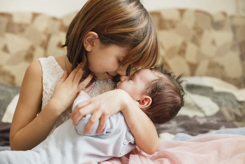 Маленькая сестра обнимая ее newborn брата Ребенк малыша встречая новый отпрыска Милая девушка и ребенок новорожденного ослабляют стоковые фото