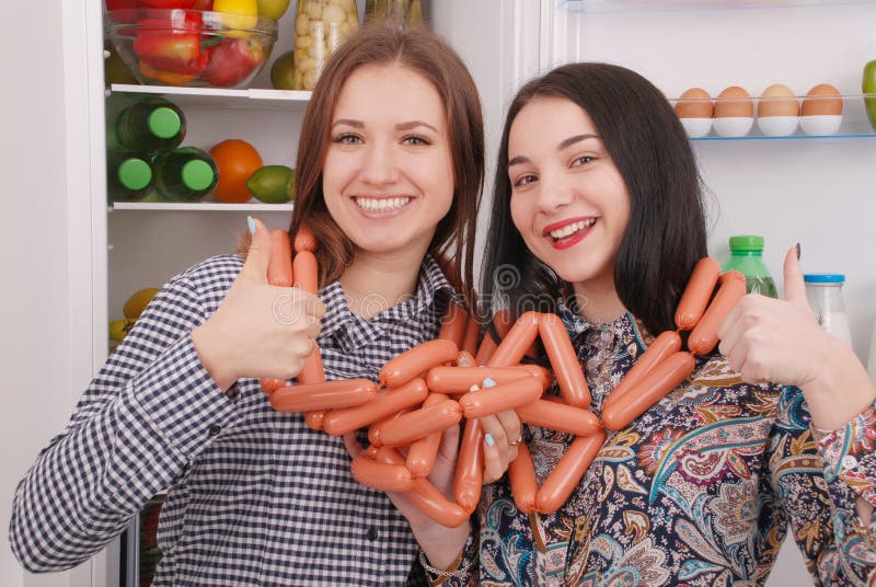 2 маленькой девочки держат сосиски на предпосылке холодильника стоковое изображение