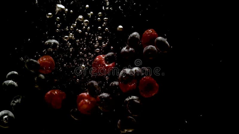 Малины и голубика strawberries брызгая в воду на черном фоне. Падающие свежие фрукты и ягоды в воде.