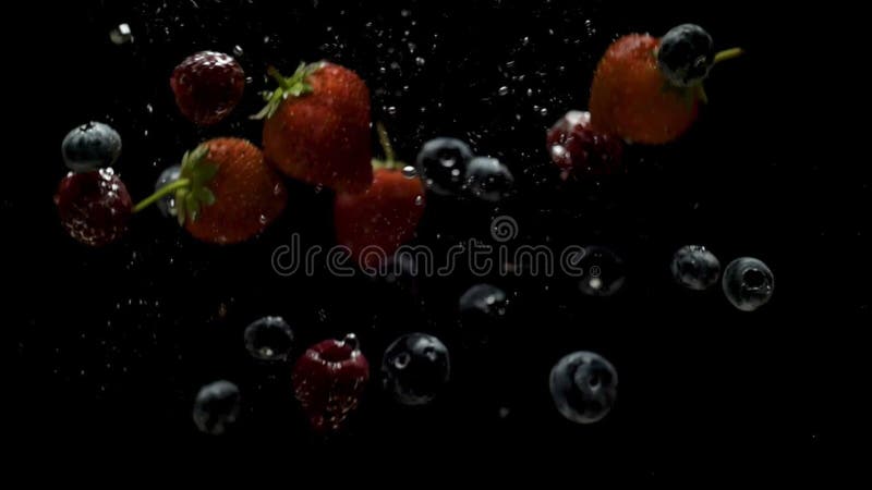 Малины и голубика strawberries брызгая в воду на черном фоне. Падающие свежие фрукты и ягоды в воде.