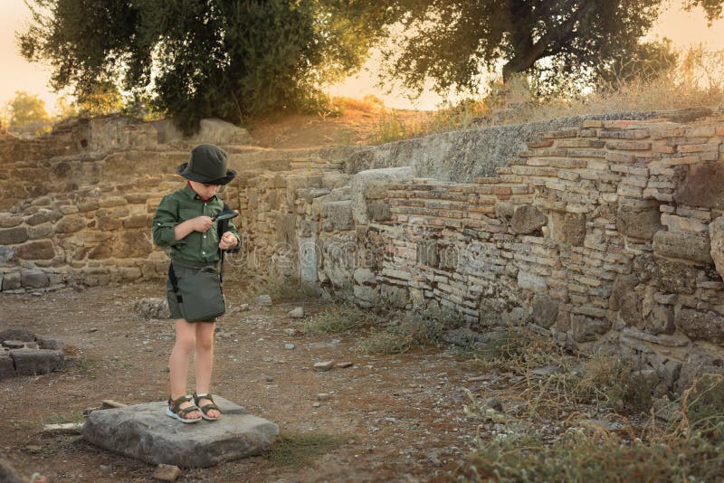 Boy archaeologist in khaki clothes studying something with magnifying glass among the ruins of an ancient city. Diverse, non-traditional jobs concept. Boy archaeologist in khaki clothes studying something with magnifying glass among the ruins of an ancient city. Diverse, non-traditional jobs concept.