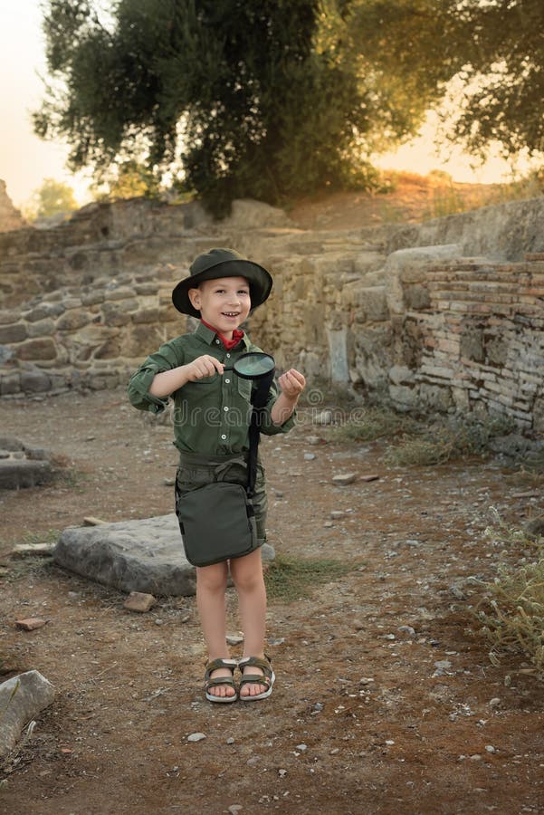 Boy archaeologist in khaki clothes studying something with magnifying glass among the ruins of an ancient city. Diverse, non-traditional jobs concept. Boy archaeologist in khaki clothes studying something with magnifying glass among the ruins of an ancient city. Diverse, non-traditional jobs concept.