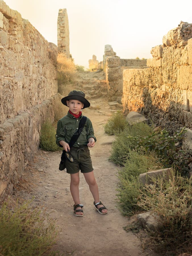 Boy archaeologist in khaki clothes studying something with magnifying glass among the ruins of an ancient city. Diverse, non-traditional jobs concept. Boy archaeologist in khaki clothes studying something with magnifying glass among the ruins of an ancient city. Diverse, non-traditional jobs concept.