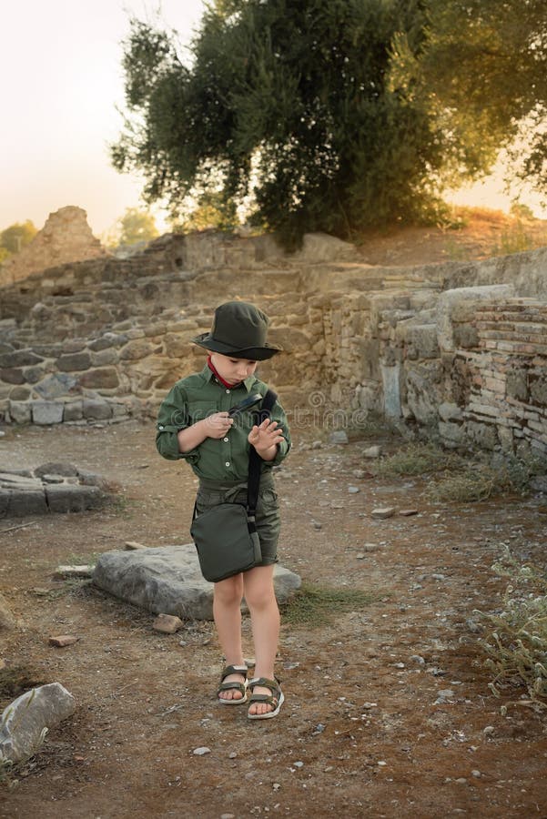 Boy archaeologist in khaki clothes studying something with magnifying glass among the ruins of an ancient city. Diverse, non-traditional jobs concept. Boy archaeologist in khaki clothes studying something with magnifying glass among the ruins of an ancient city. Diverse, non-traditional jobs concept.