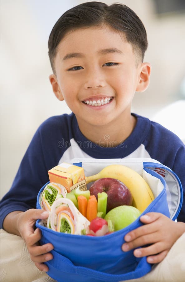 Young boy indoors with packed lunch smiling. Young boy indoors with packed lunch smiling