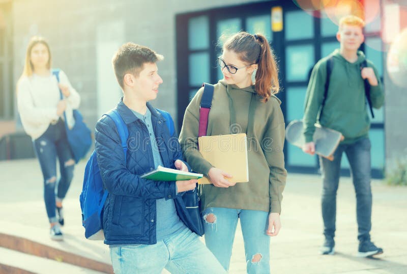 Positive teenage friends discuss past lessons on the street near college building. Positive teenage friends discuss past lessons on the street near college building