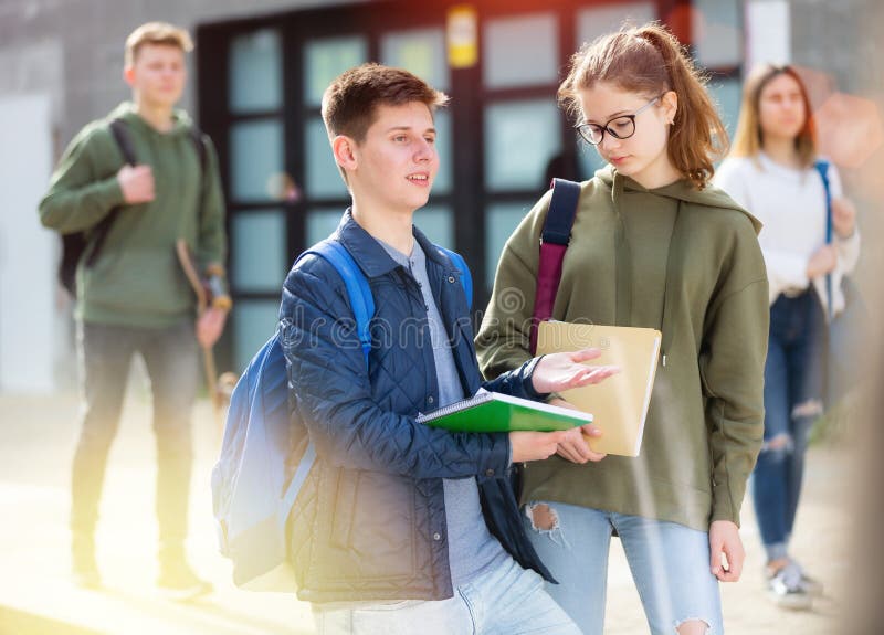 Cute teen girl with workbooks in hands walking with her classmate outside college building. Cute teen girl with workbooks in hands walking with her classmate outside college building