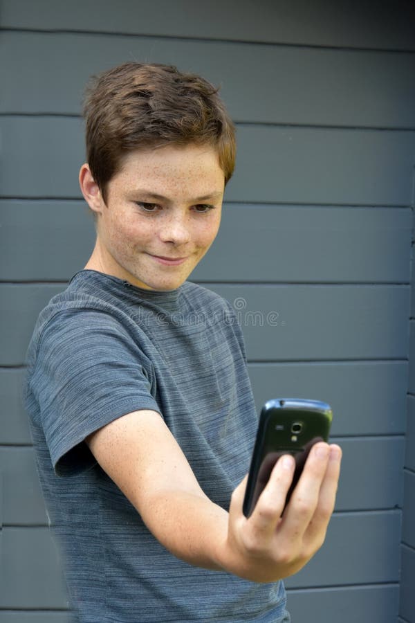 Teenage boy using his mobile phone, reads a text message, makes a selfie. Teenage boy using his mobile phone, reads a text message, makes a selfie
