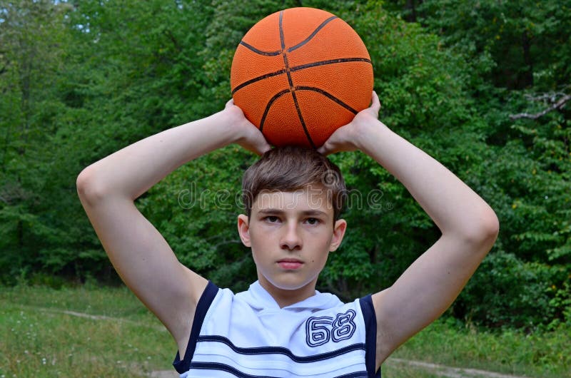 Мальчик подростка в белой рубашке без рукавов с шариком для баскетбола ...