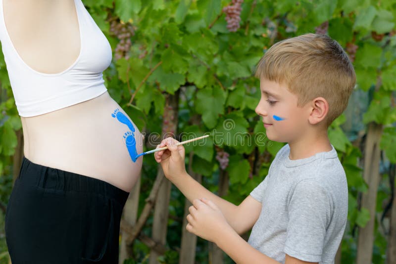 Мальчик рисует с щеткой на животе его беременного следа ноги baby’s мамы Беременная концепция : стоковое изображение rf Мальчик рисует с щеткой на животе его беременного следа ноги baby’s мамы Беременная концепция : стоковое изображение rf