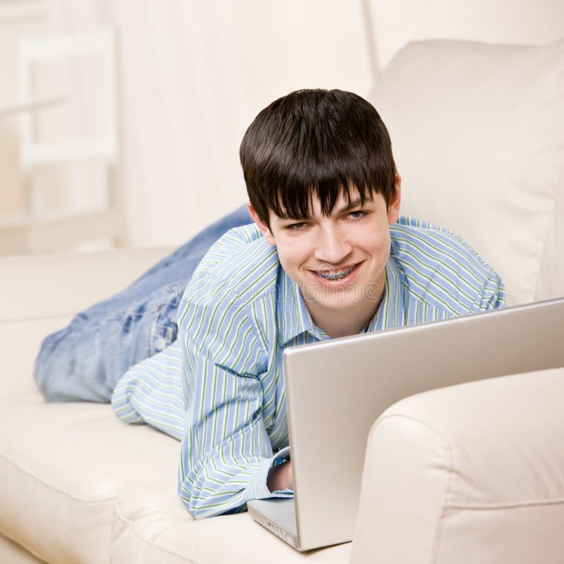 Boy with braces relaxing on sofa in livingroom using laptop for internet. Boy with braces relaxing on sofa in livingroom using laptop for internet